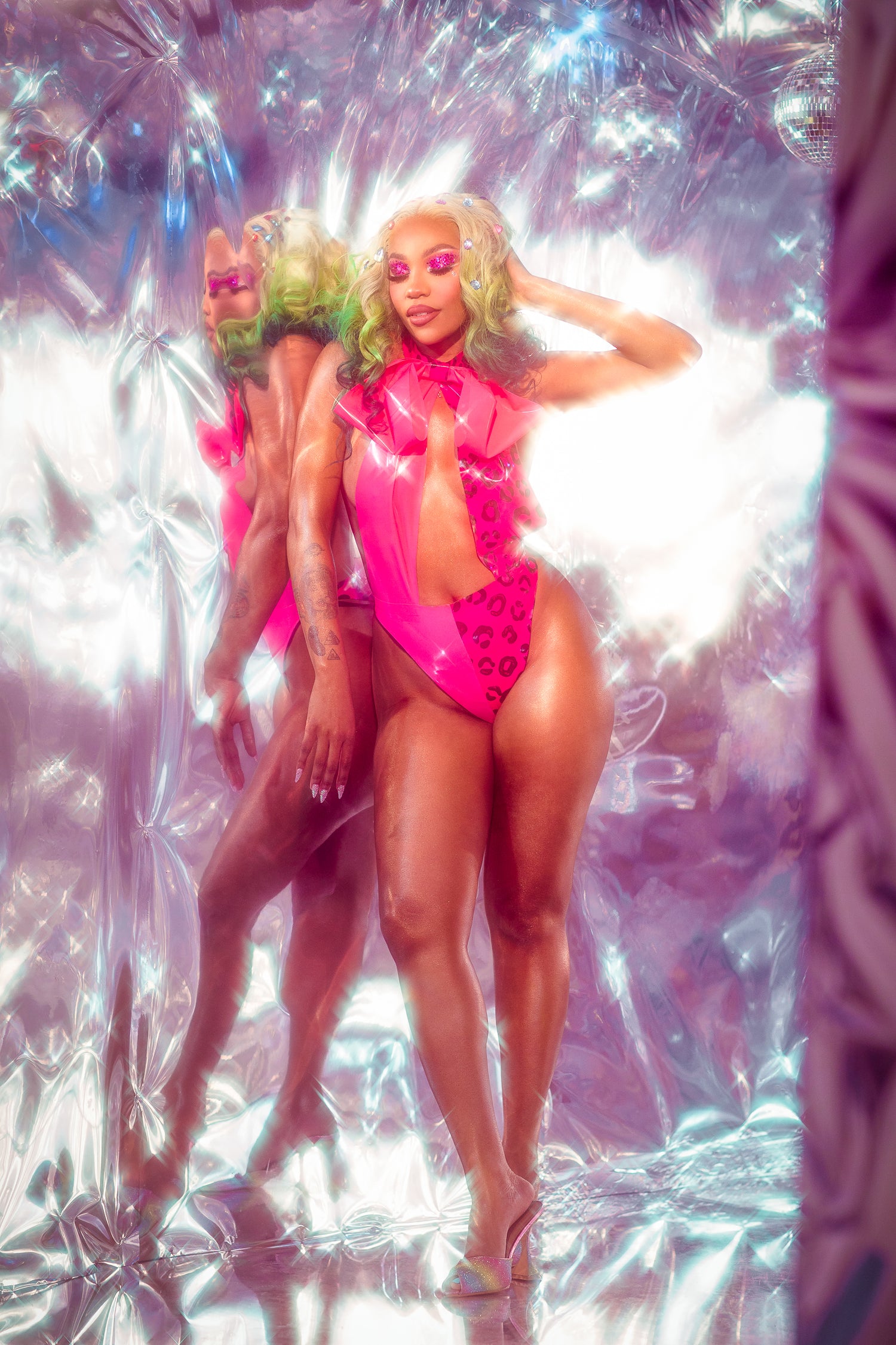 model in shiny pink outfits posing against a reflective silver background.