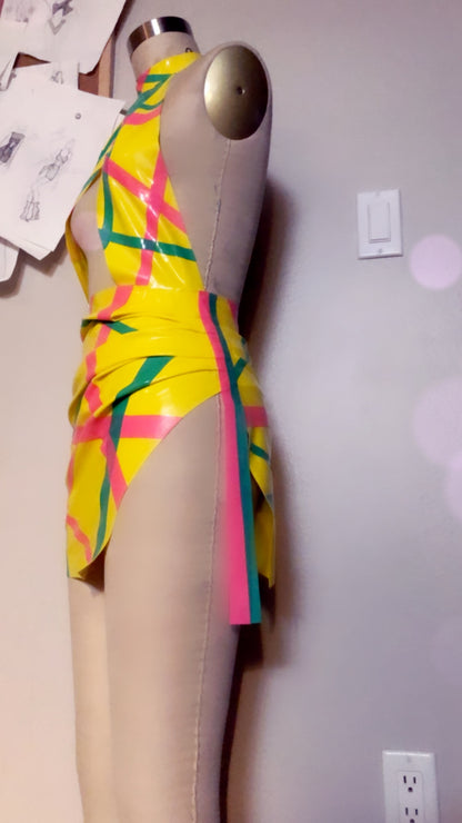 Colorful latex dress on a mannequin against a plain wall, side view.