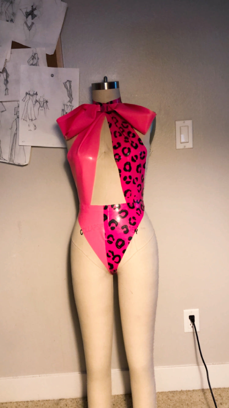 Mannequin wearing a pink swimsuit with leopard print details against a plain wall.
